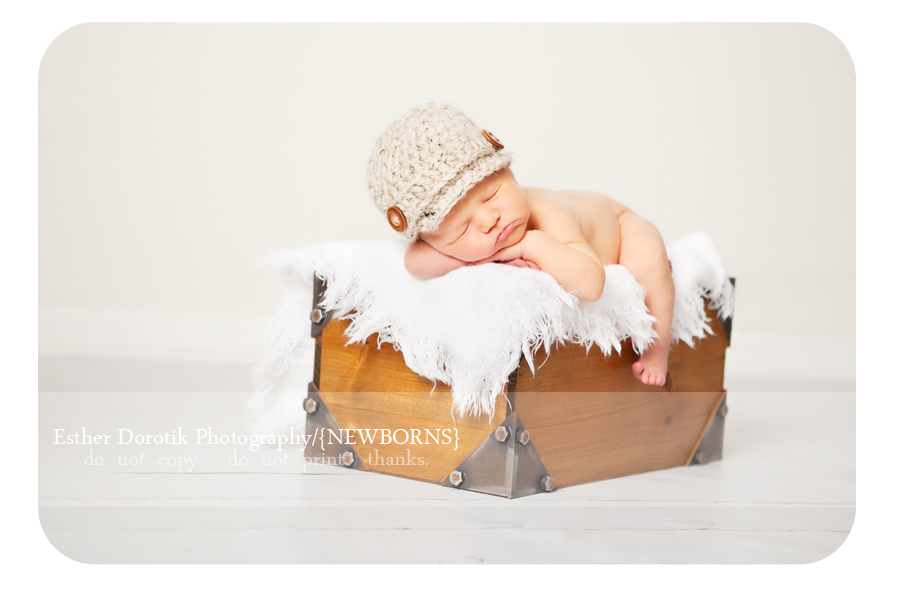 newborn-baby-boy-lying-on-blanket-with-newsboy-hat-and-leg-hanging-off-basket